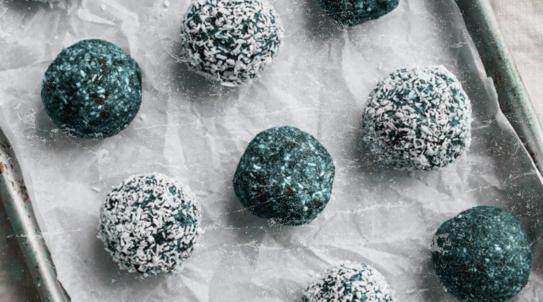 Blue Cocos Energy Balls on a parchment-lined tray—some rolled in shredded coconut, showcasing a vibrant blue-green hue from Elyxar superfood blend.