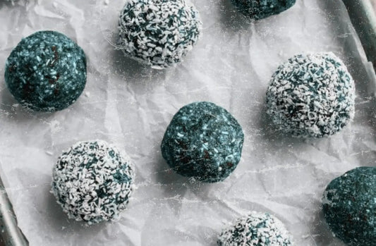 Blue Cocos Energy Balls on a parchment-lined tray—some rolled in shredded coconut, showcasing a vibrant blue-green hue from Elyxar superfood blend.