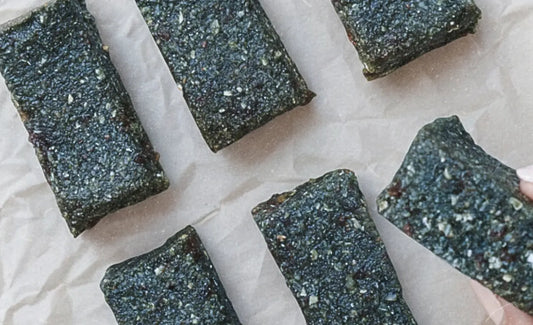 Hand holding a superfood-packed Oatmeal Date Bar made with Elyxar—dark, chewy bars arranged on parchment paper for a nutritious, no-bake snack.